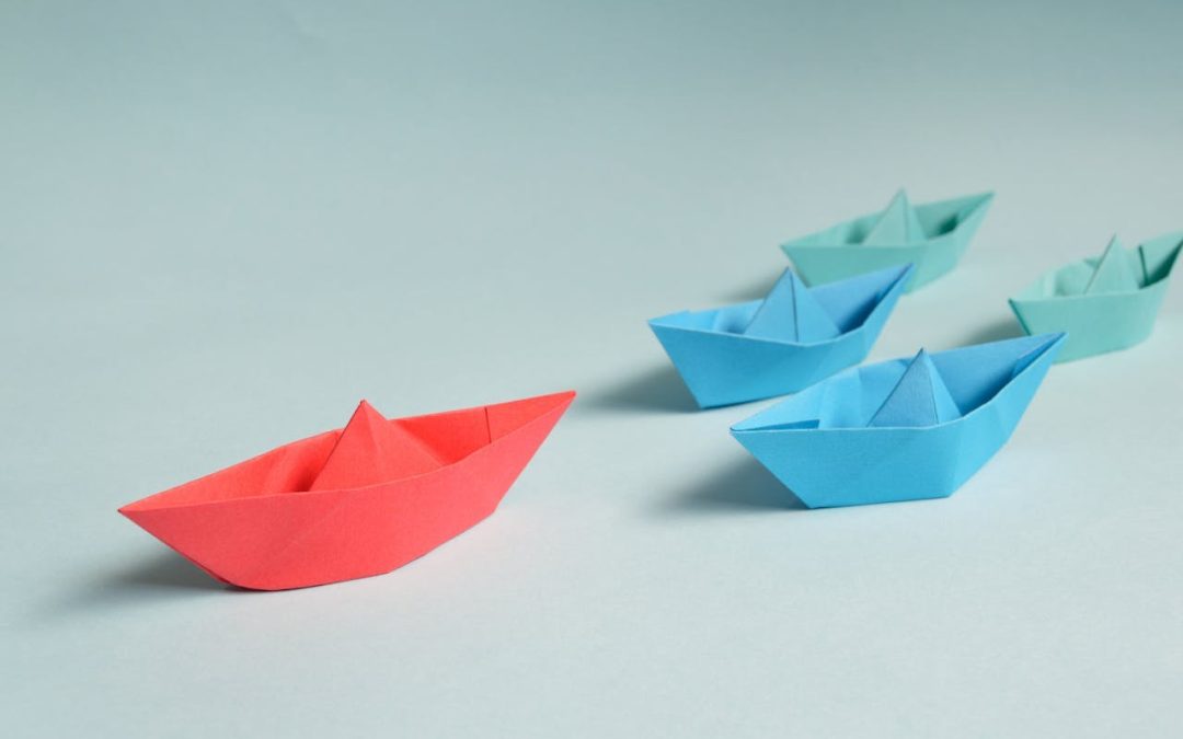 Colorful paper boats with a red boat leading the way