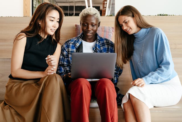 Three friends sitting and smiling while looking at a laptop together.